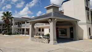 A building with a covered entrance, a tower with a blue roof, and a palm tree in the foreground. - Summit Inn - Houston Medical Center (Houston)