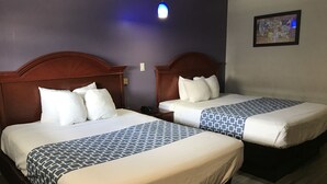 A hotel room with two beds, each with a wooden headboard, white bedding, and a patterned throw. A single bed has a phone on the nightstand. - Summit Inn - Houston Medical Center (Houston)