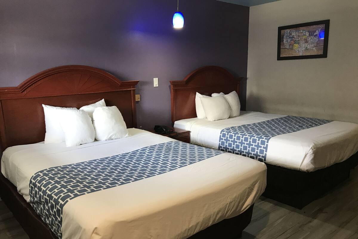 Quarto de hotel com duas camas, cada uma com cabeceira de madeira, roupa de cama branca e manta estampada. Uma das camas tem um telefone na mesinha de cabeceira.