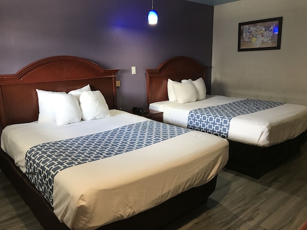 Habitación de hotel con dos camas, cada una con cabecero de madera, ropa de cama blanca y una manta estampada. Una de las camas tiene un teléfono en la mesita de noche.