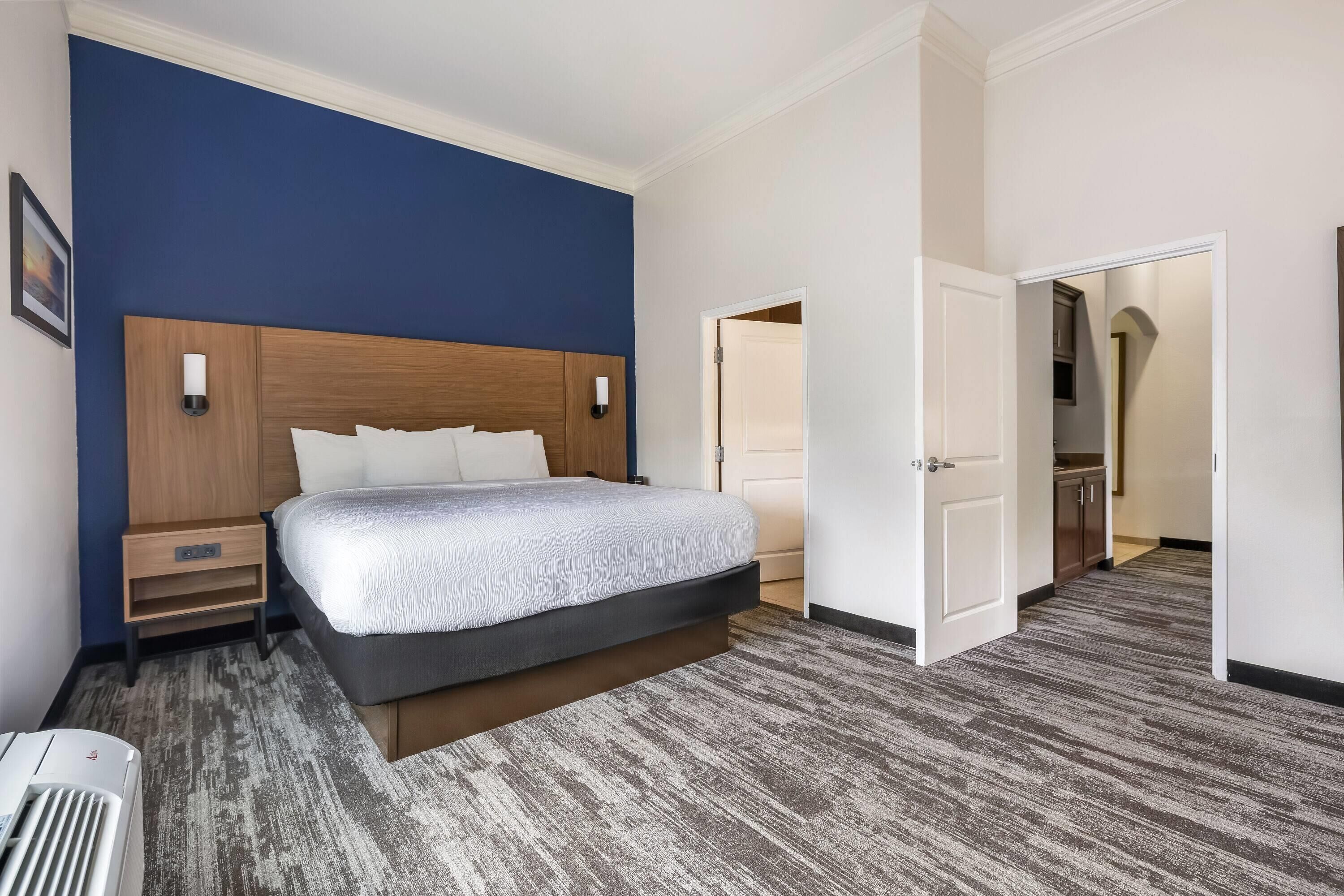 A hotel room with a bed, bedside tables, a nightstand, a wall-mounted lamp, and a carpeted floor.