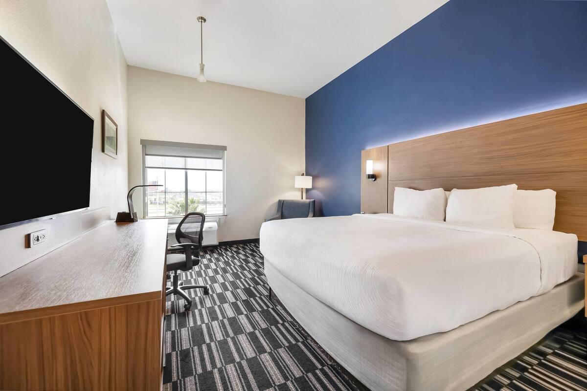 Ein Hotelzimmer mit einem großen Bett, einem Schreibtisch, einem Flachbildfernseher, einem Fenster und einer blauen Akzentwand.
