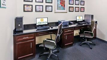 A hotel reception area with two computer stations, a desk, chairs, and framed artwork on the wall.