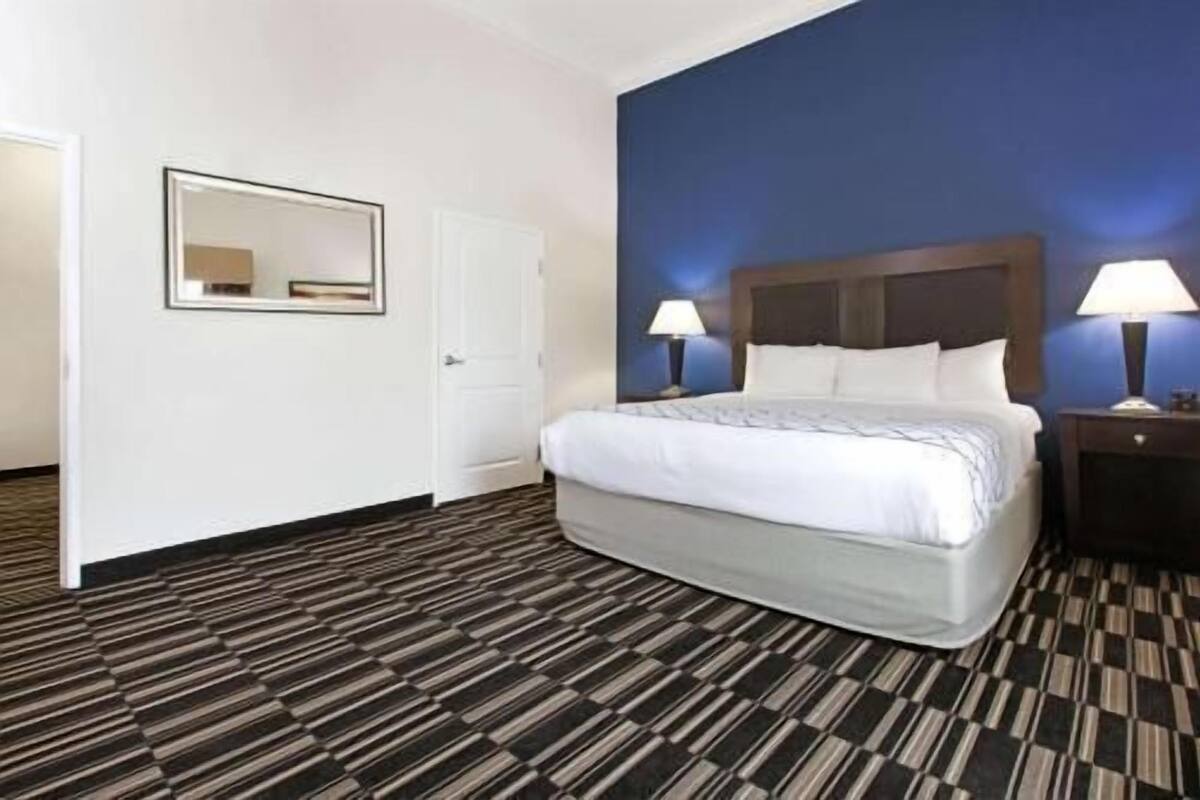 Ein Hotelzimmer mit einem Bett, zwei Nachttischen mit Lampen, einem Spiegel und einem gemusterten Teppich.