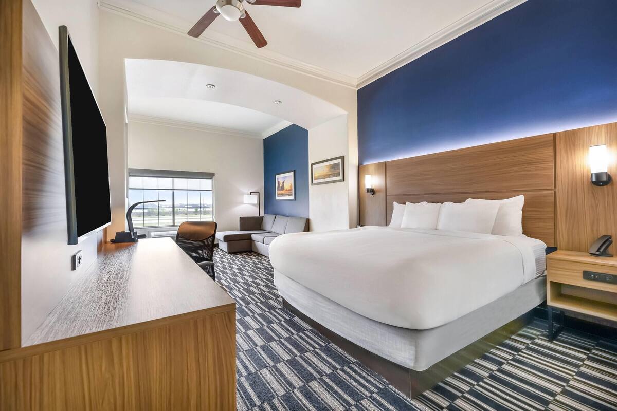 Ein Hotelzimmer mit einem großen Bett, einem Schreibtisch, einem Stuhl, einem Fernseher, einem Deckenventilator und einem Fenster mit Blick.