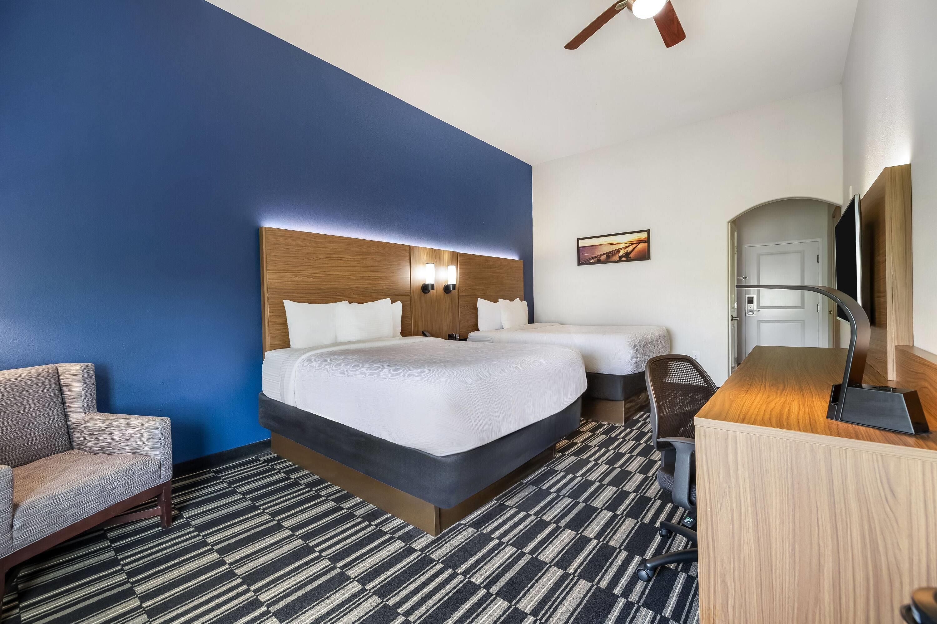 Habitación de hotel con una cama grande, un escritorio, una silla y un ventilador de techo.