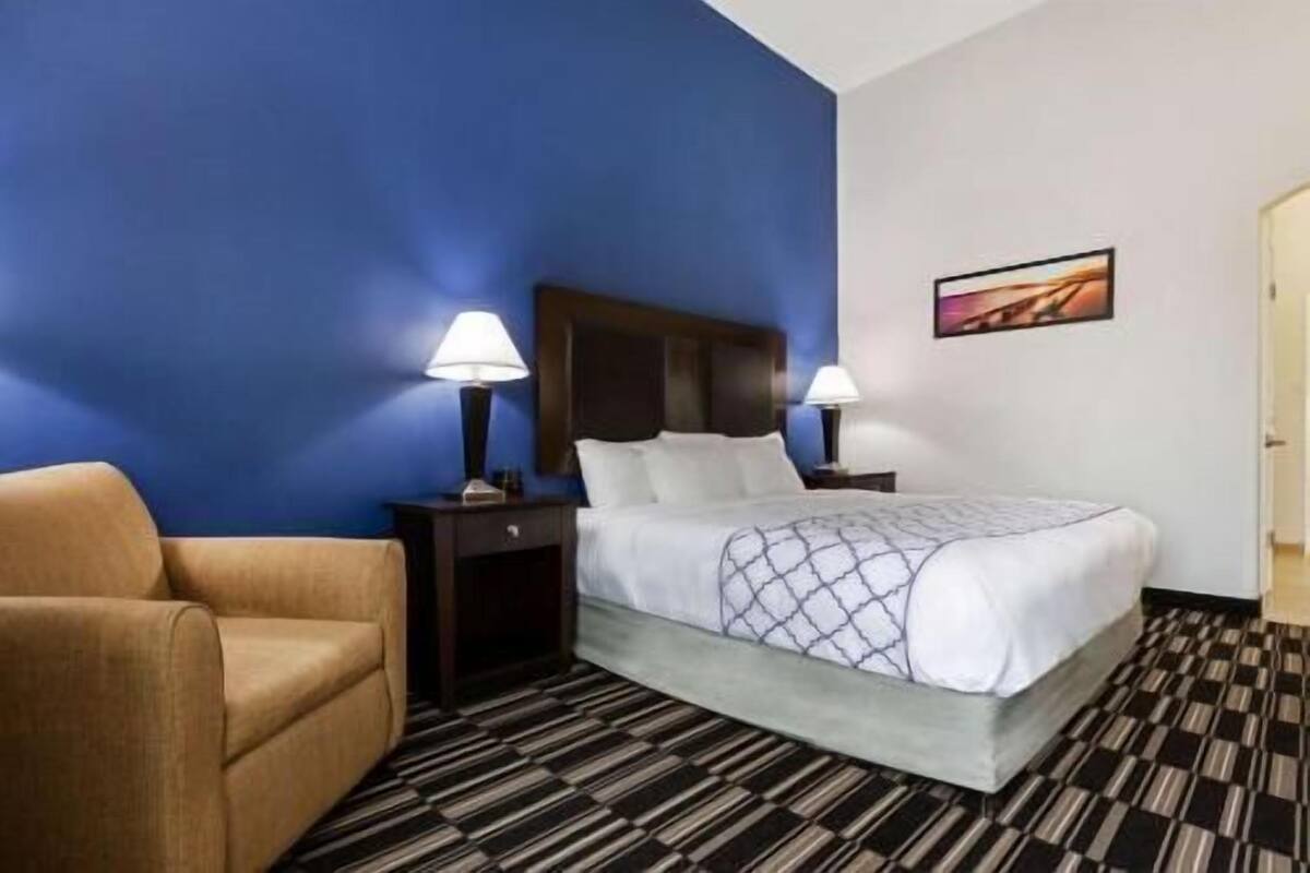 Ein Hotelzimmer mit einem Bett, zwei Nachttischlampen, einem Sessel und einem Bild an der Wand.
