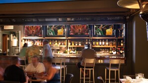 Zona de bar con diferentes disposiciones de asientos y una barra repleta de diversas botellas.