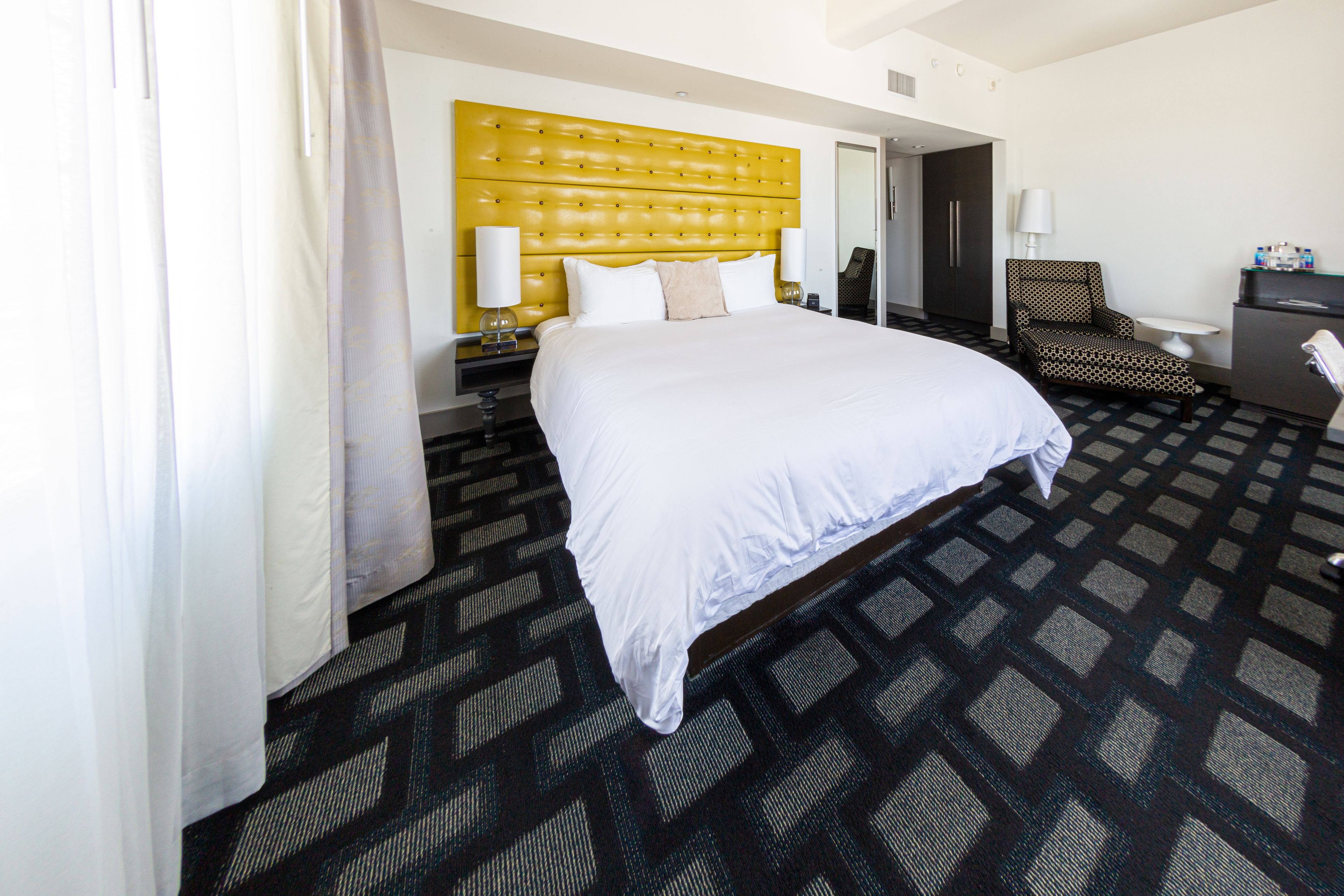 A hotel room with a large bed, a headboard, a chair, a desk, and a mirror.