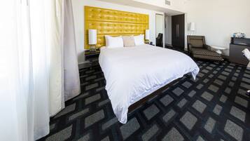 A hotel room with a large bed, a headboard, a chair, a desk, and a mirror.