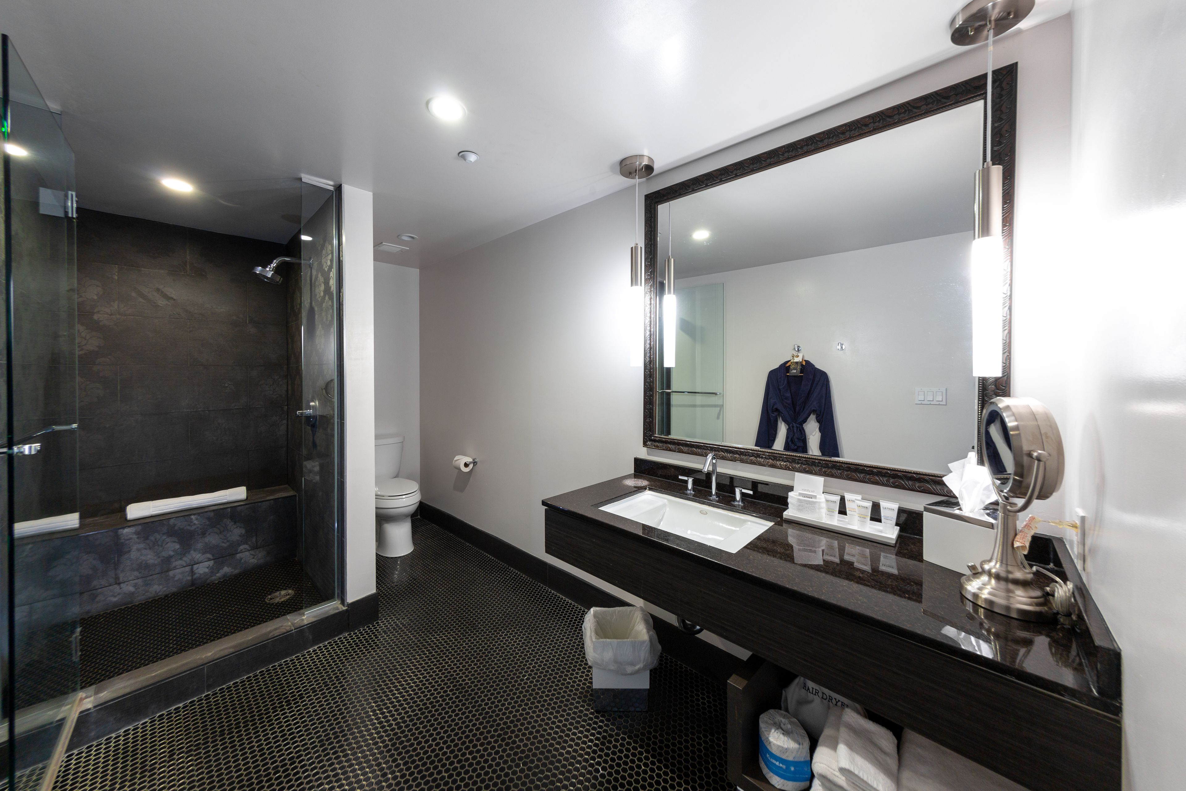 Un baño moderno con ducha de vidrio, un espejo grande y encimera oscura.