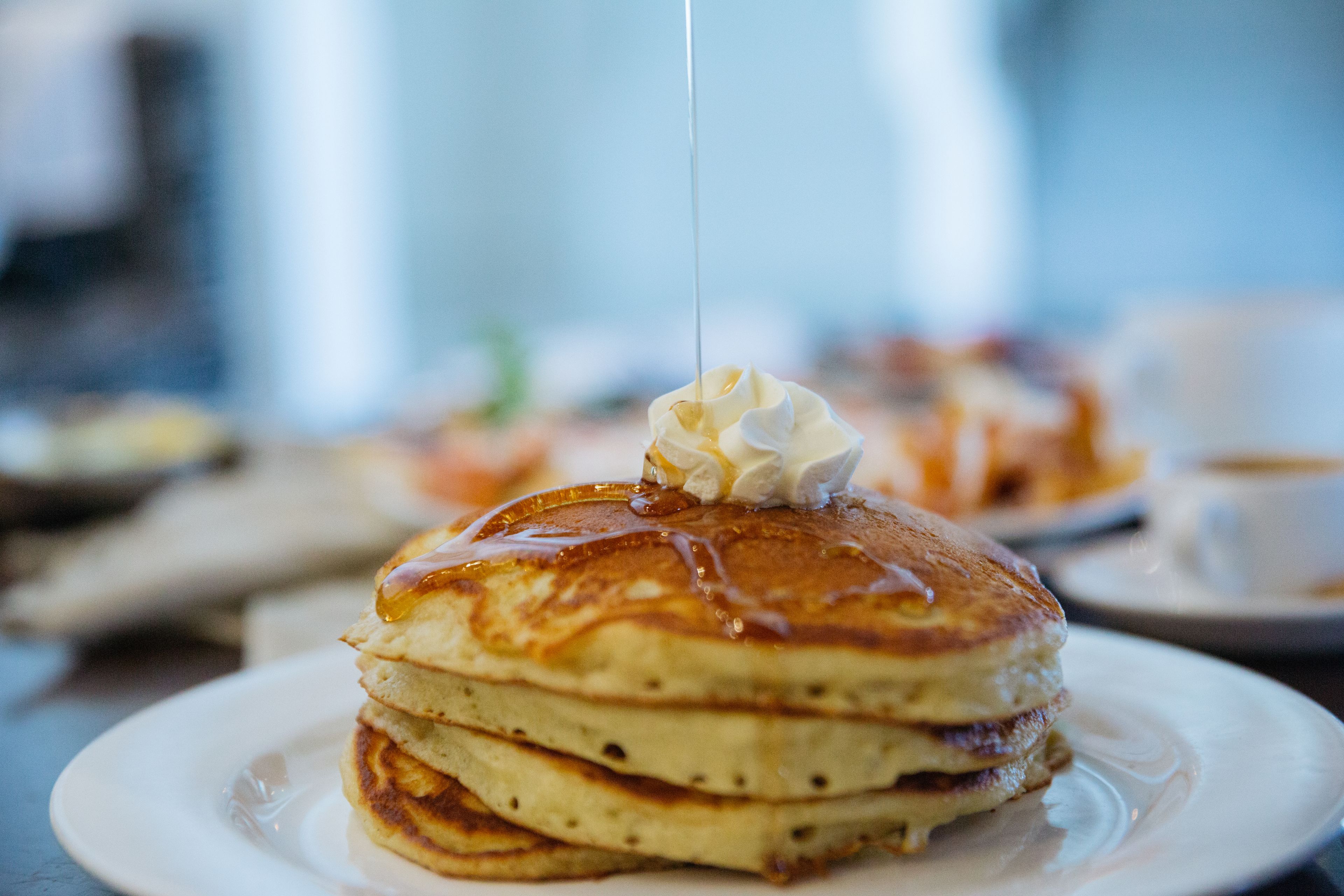 A stack of pancakes with syrup and whipped cream on a plate.