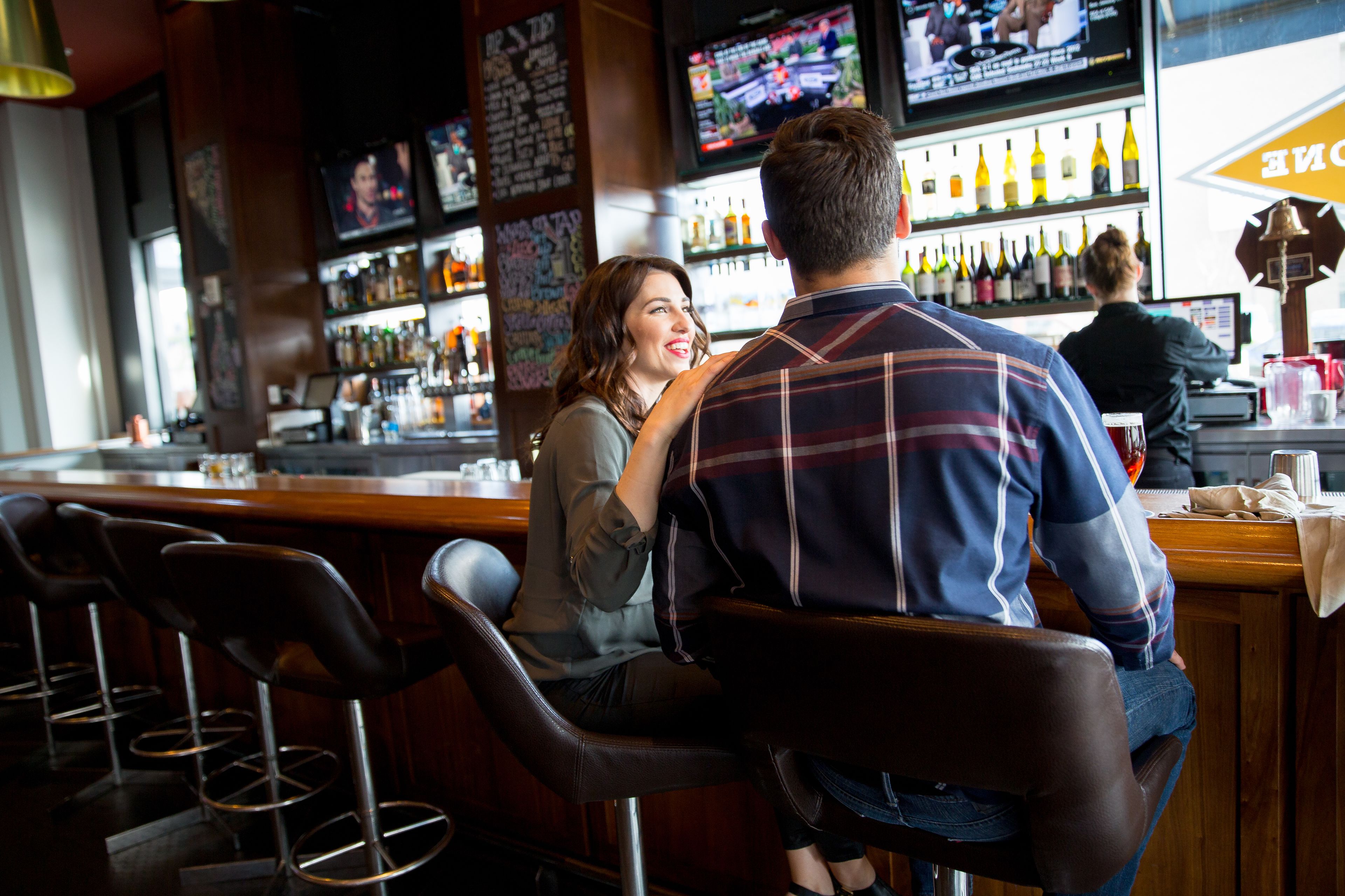 A bar with a counter, stools, and a television screen.