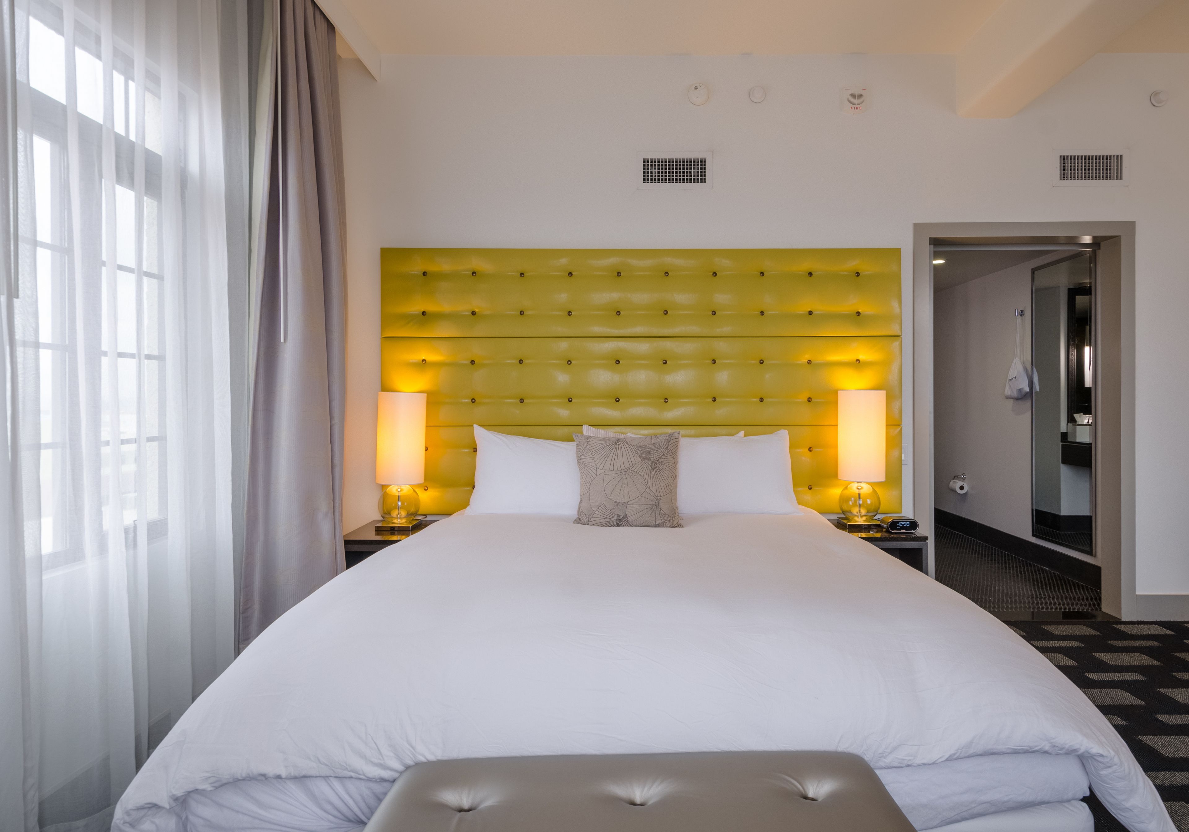 A hotel room with a large bed, a tufted headboard, two bedside lamps, and a visible bathroom door.