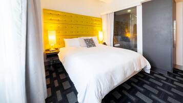 A hotel room with a large bed, a yellow headboard, a glass door leading to a balcony, and a patterned carpet.