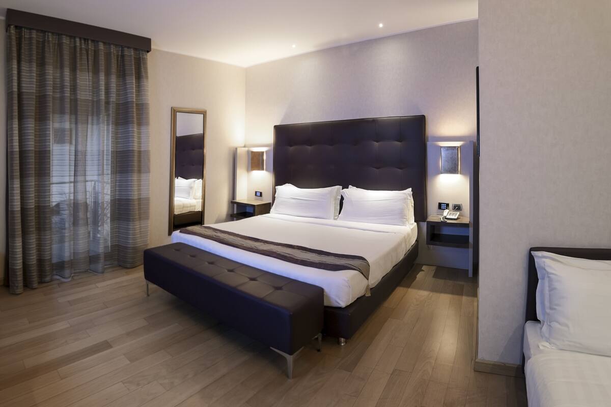 Una habitación de hotel moderna con una cama grande, mesitas de noche, un banco y un espejo.