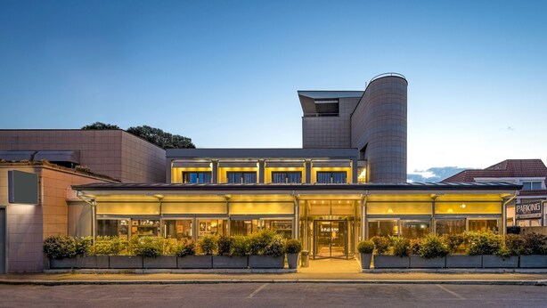 A modern hotel with a prominent cylindrical tower, large glass windows, and a well-lit entrance. - Rome Airport Hotel Fiumicino (Fiumicino)