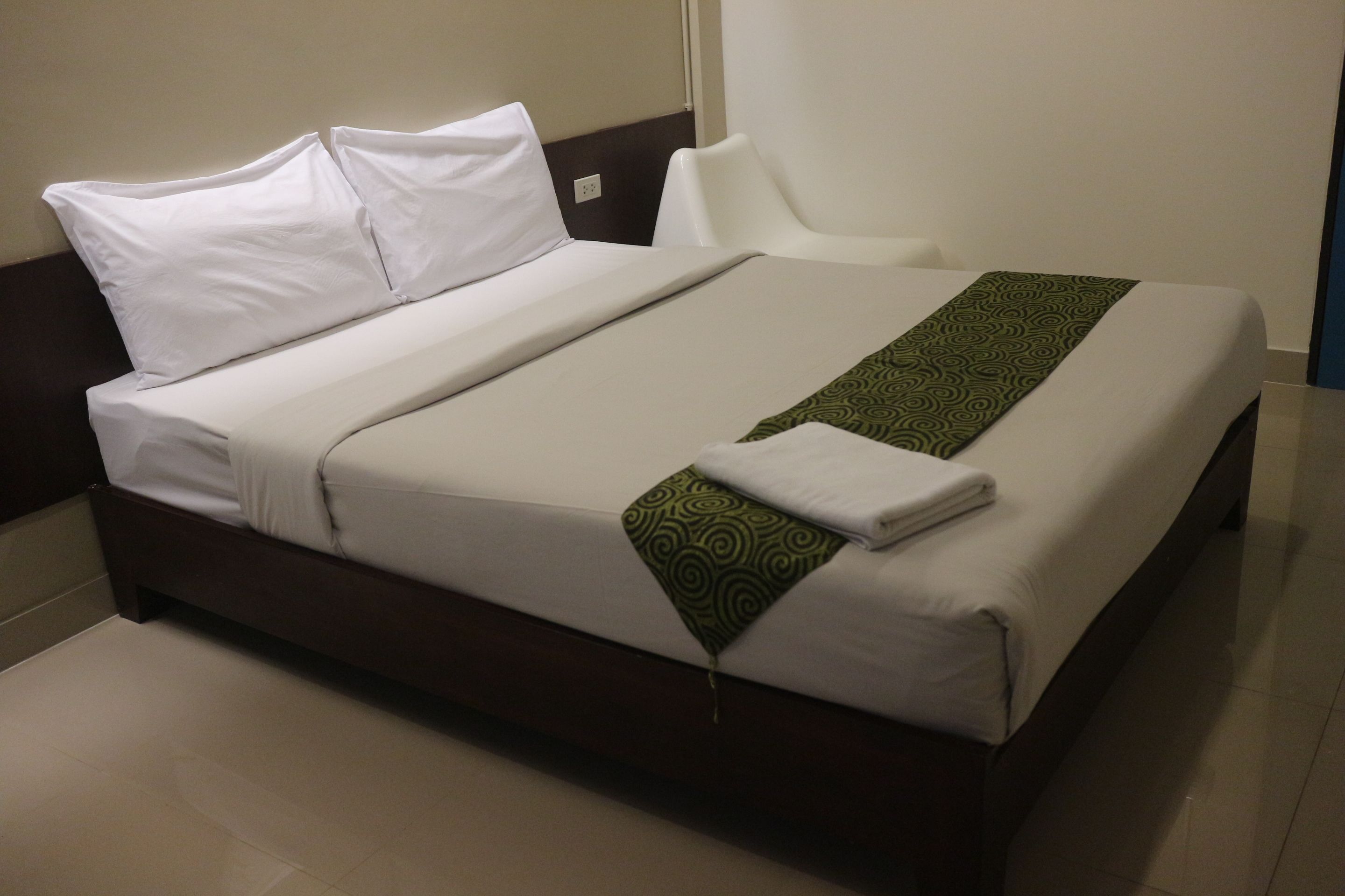 Un letto rifatto con lenzuola bianche e una coperta verde fantasia.