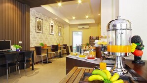 A hotel breakfast area with a fruit display, a juice dispenser, and a seating area with chairs and tables. - Floral Shire Resort (Bangkok)