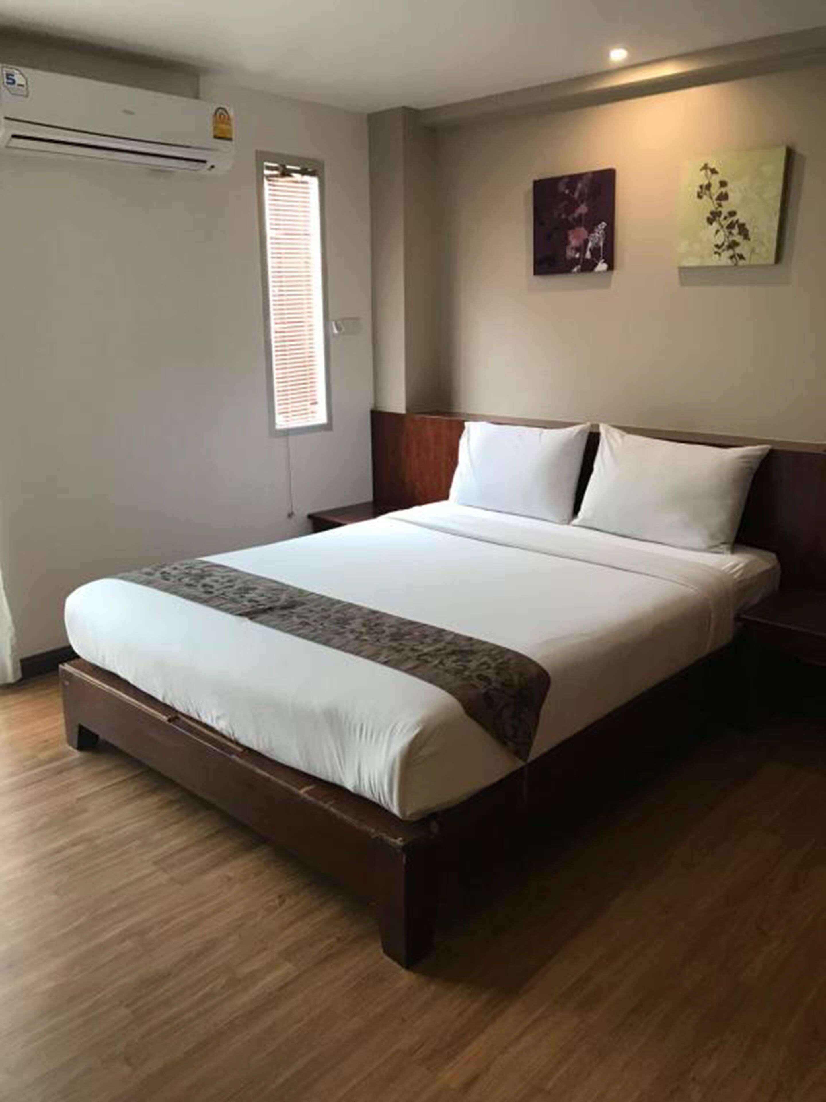 A neatly made bed with a wooden headboard, a bedside table, and a wall-mounted air conditioner.
