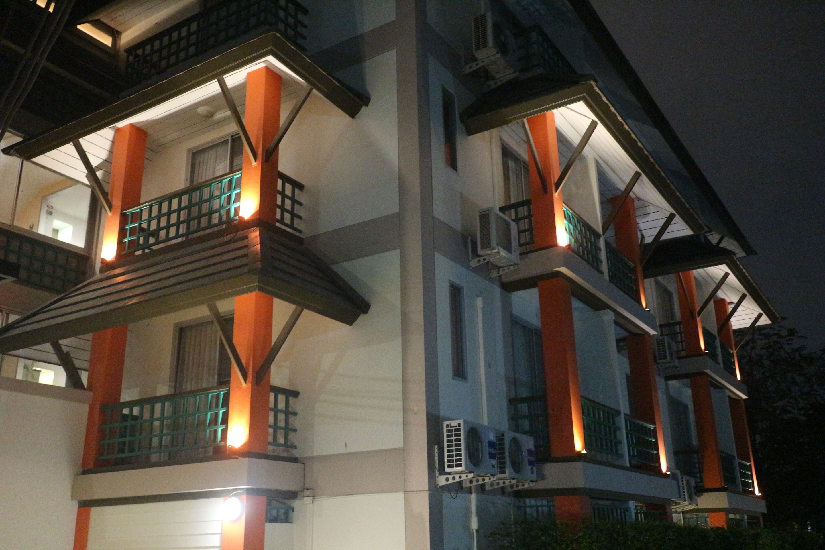 A multi-story building with balconies, air conditioning units, and a night-time setting.