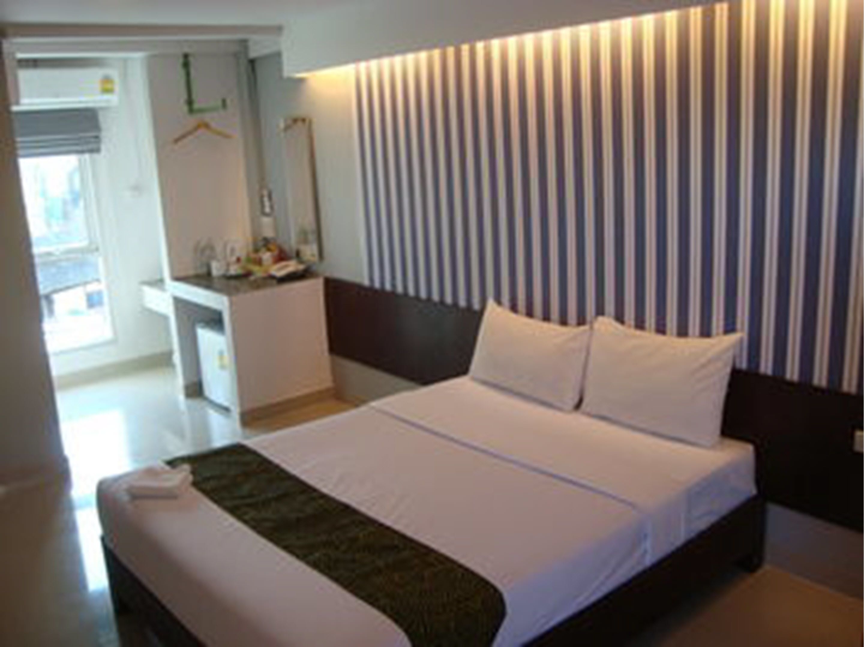 Habitación de hotel moderna con una cama grande, una mesita de noche, un espejo y un panel de pared a rayas.