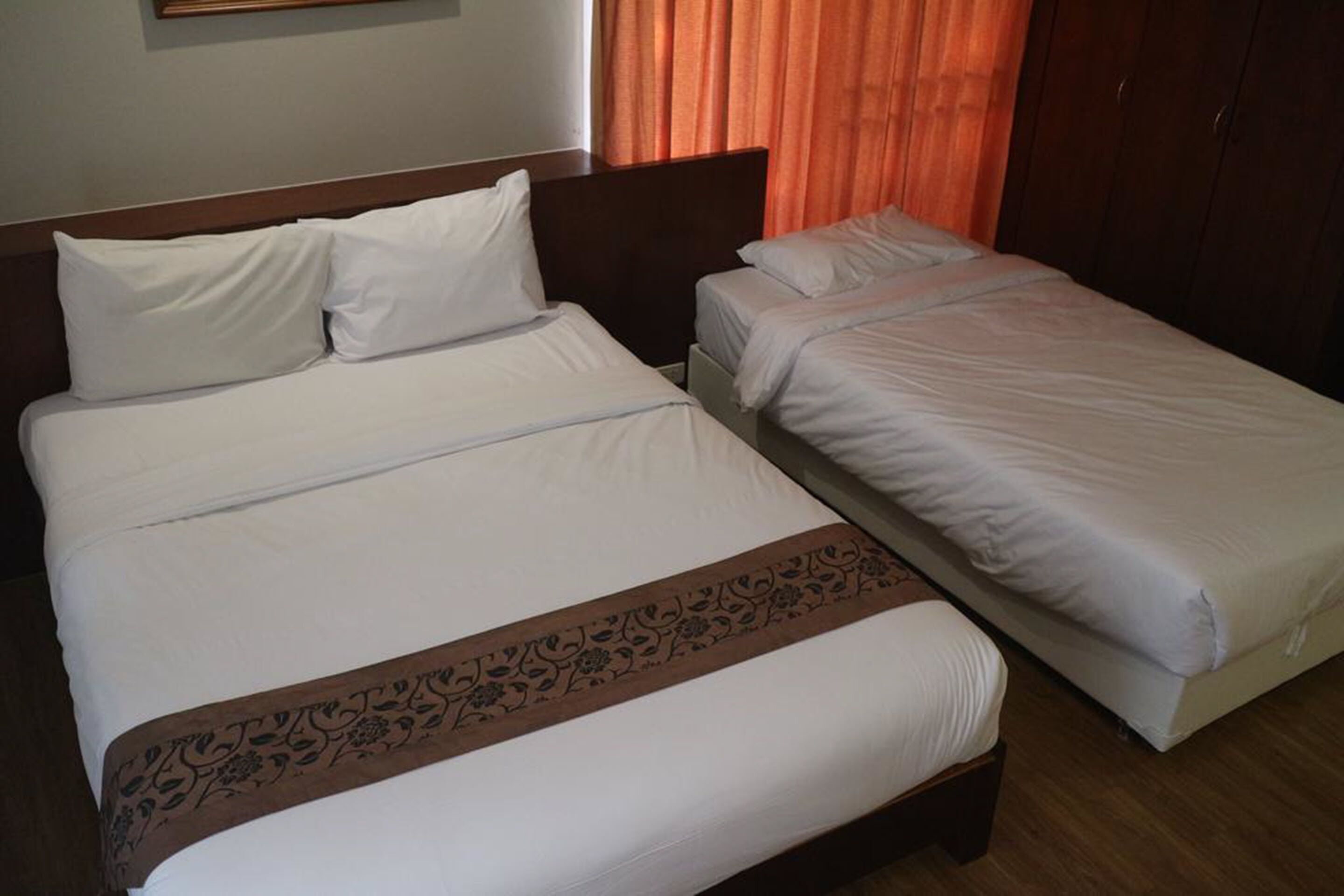 A double bed with a decorative headboard and a single bed with a plain headboard in a hotel room.