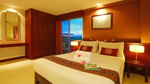 A hotel room with a large bed, a nightstand, a mirror, and a view of the city at dusk. - Floral Shire Resort (Bangkok)