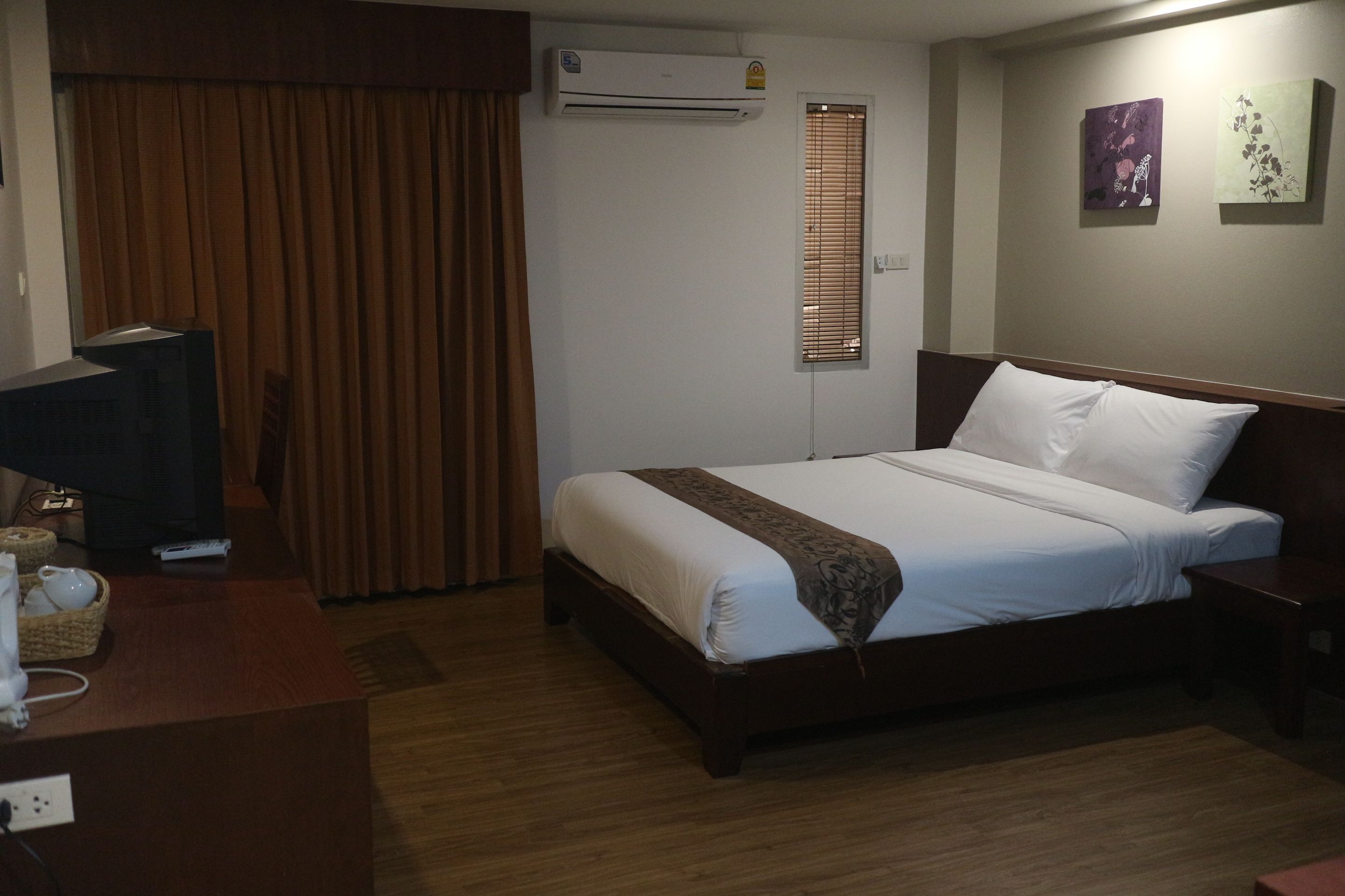 A hotel room with a bed, a television, a desk, and an air conditioning unit.