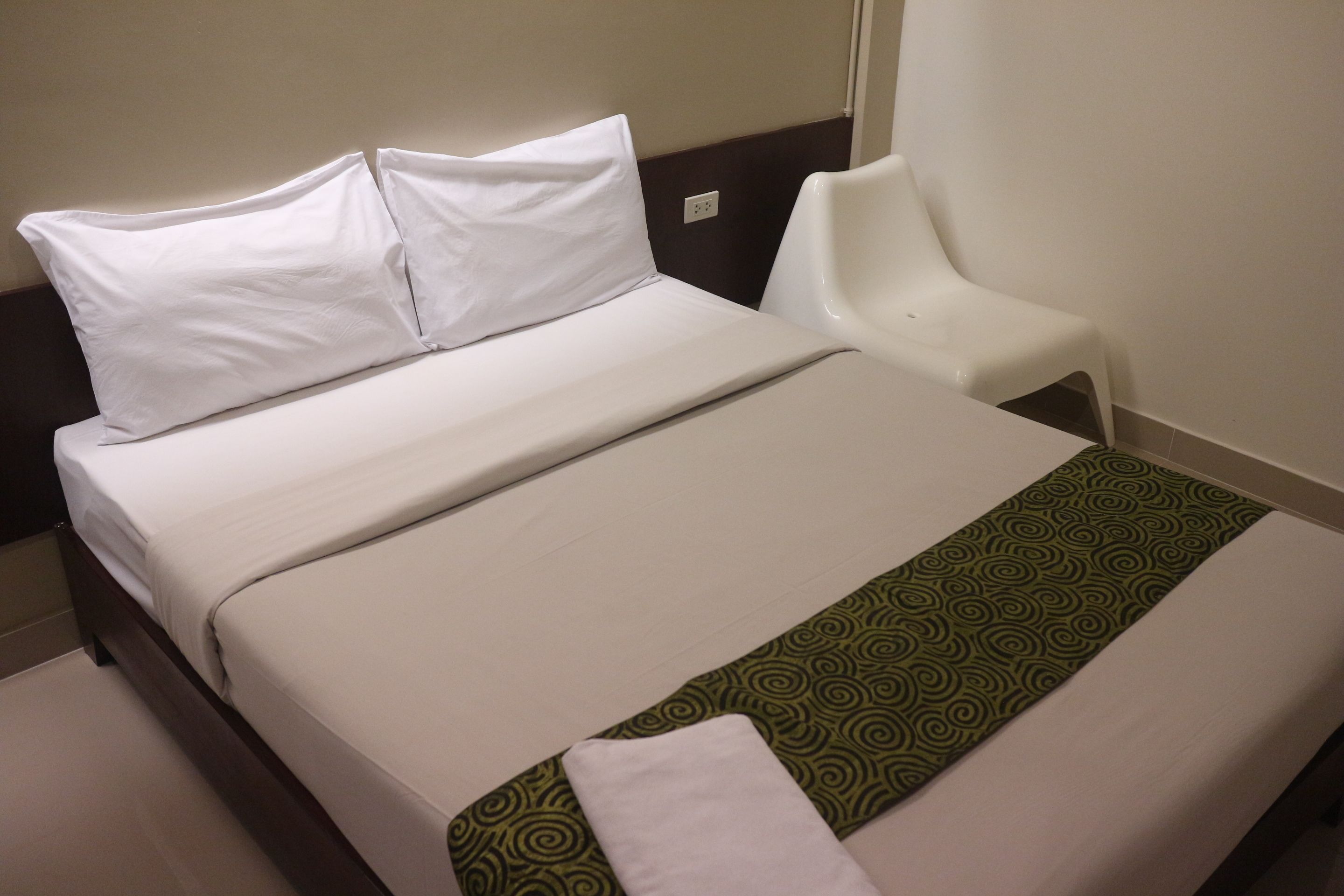 A neatly made bed with white linens and a green patterned runner.