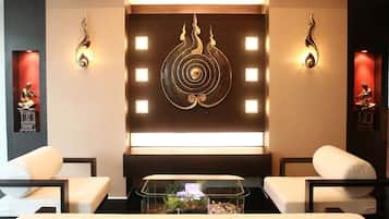 A modern room with two white sofas, a glass coffee table with decorative items, and wall-mounted light fixtures.