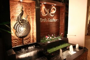 A water feature with a peacock sculpture and a sign reading "Tirth Sathon".