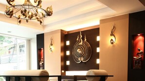A modern lobby with a reflective floor, two sofas, a chandelier, and wall art. - Mirth Sathorn Hotel (Bangkok)