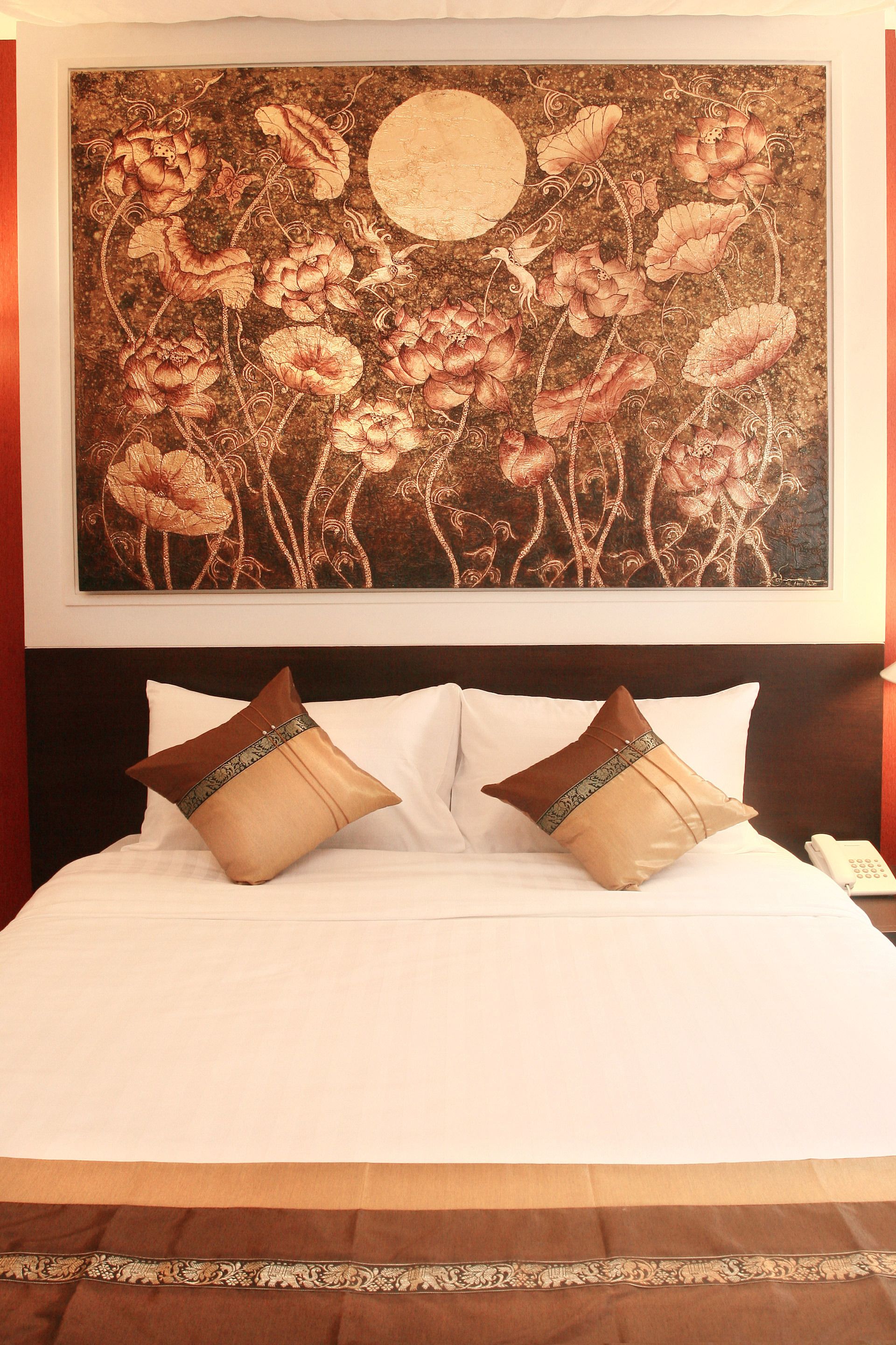 A hotel room with a bed, two pillows, and a large floral artwork above the bed.