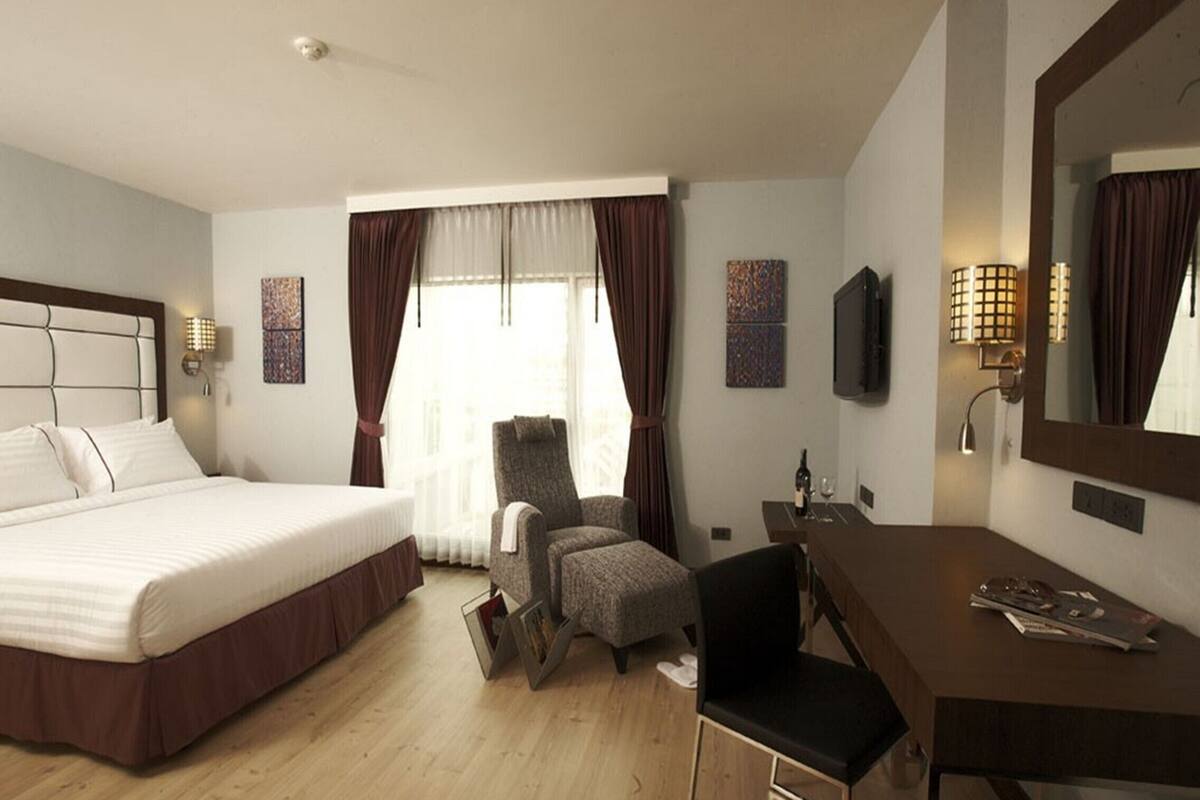 Ein Hotelzimmer mit einem großen Bett, einem Schreibtisch, einem Sessel, einem Fernseher und einem Fenster mit Vorhängen.