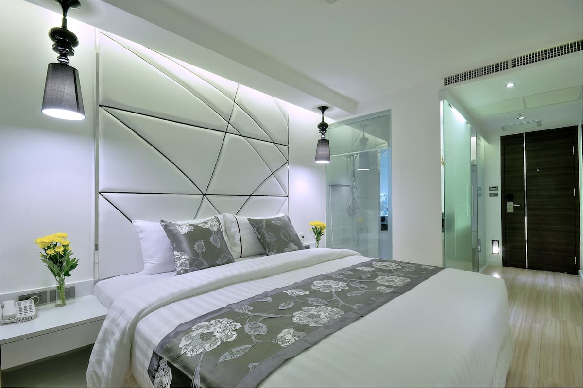 Ein modernes Schlafzimmer mit einem geometrischen Kopfteil, einem großen Bett mit floraler Bettdecke, Nachttischen mit Lampen und einer Duschkabine aus Glas.