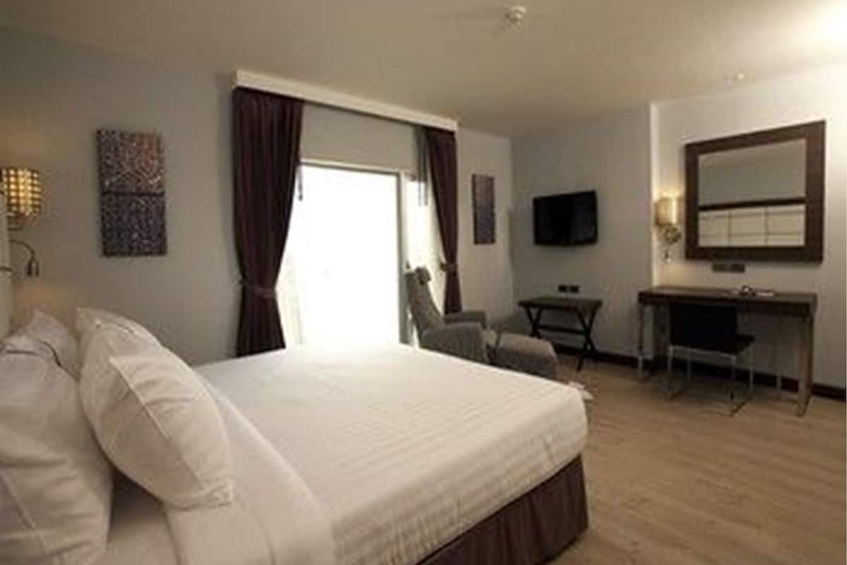 Ein Hotelzimmer mit Bett, Schreibtisch, Stuhl, Fernseher und einem fenster mit Vorhängen.