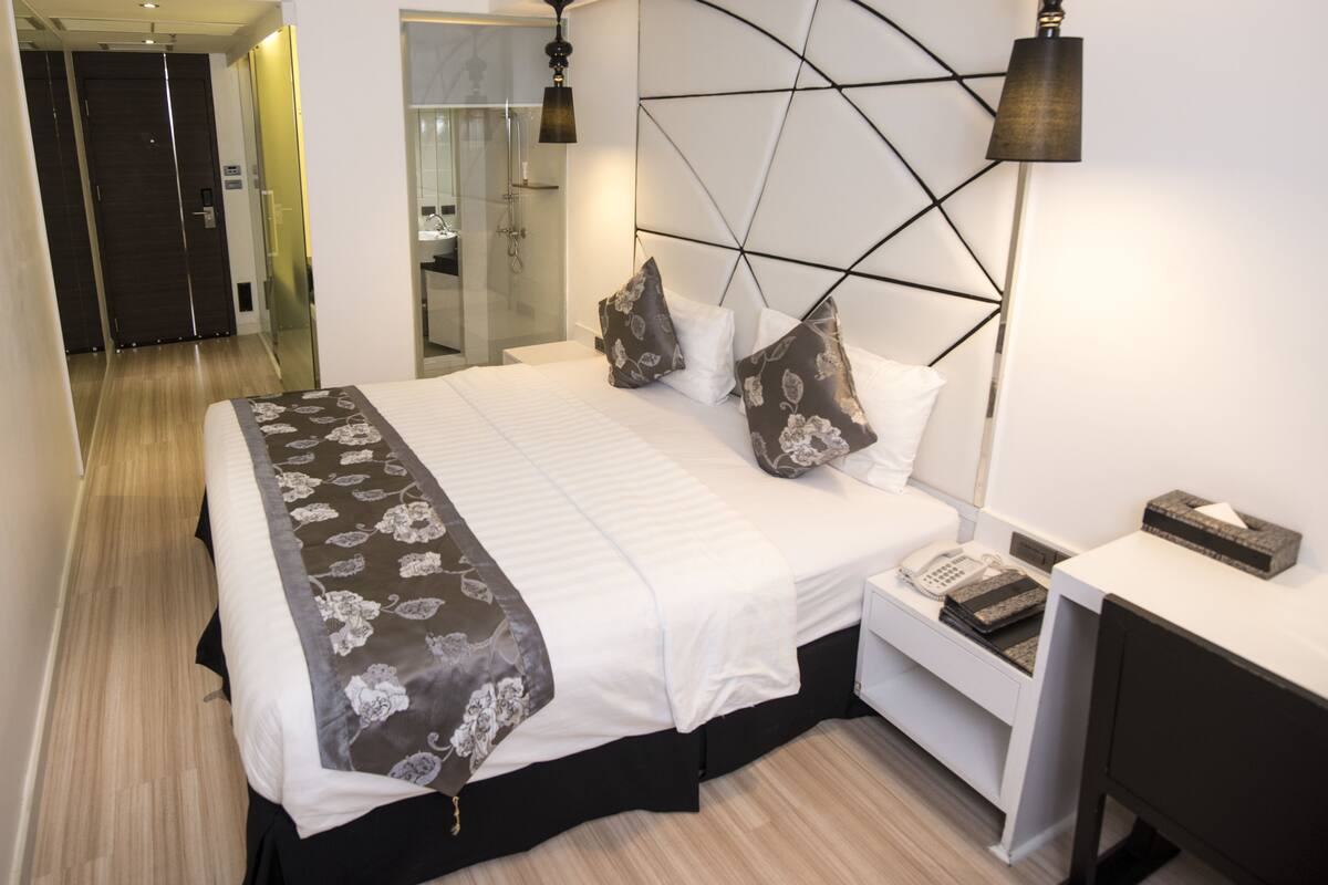 Ein modernes Hotelzimmer mit einem großen Bett, einem Nachttisch mit Telefon und einem Beistelltisch mit Lampe.
