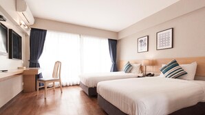 Une chambre d’hôtel avec deux lits, un bureau, une chaise et une grande fenêtre avec des rideaux.