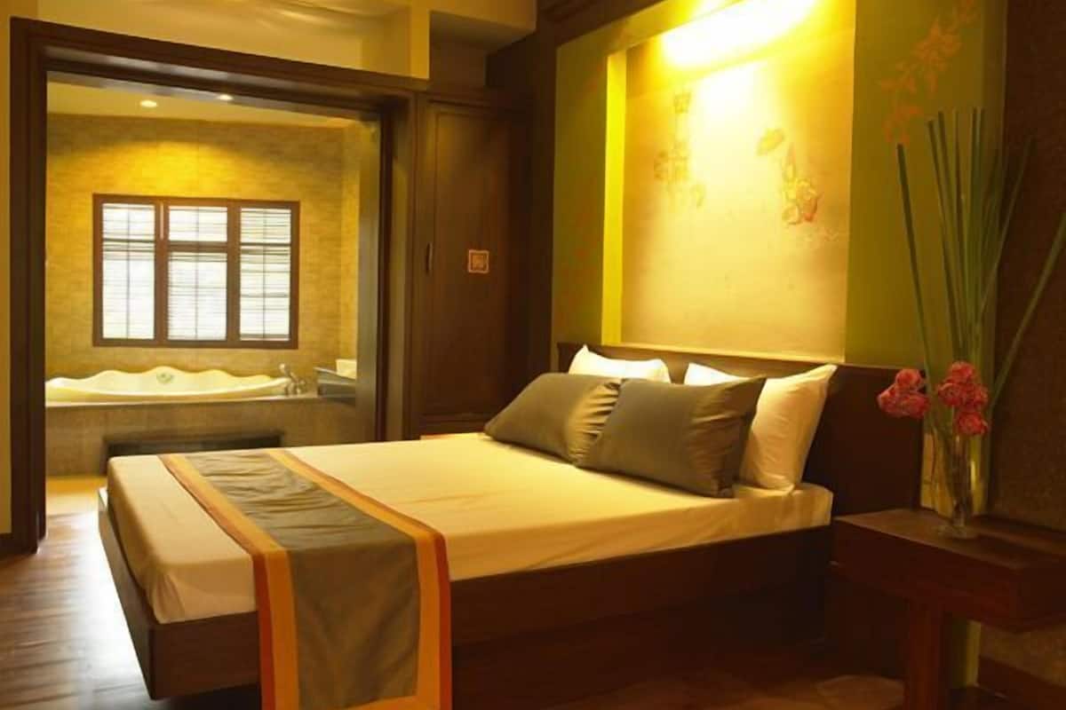 Une chambre avec un grand lit, une table de chevet, une commode, une lampe fixée au mur et une fenêtre donnant sur une salle de bain.