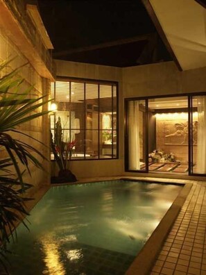 Une piscine avec une terrasse carrelée, un mur en pierre et une grande fenêtre équipée de stores.