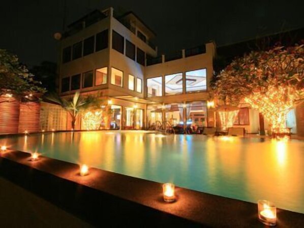 A modern building with a pool, surrounded by trees and lit by candles.