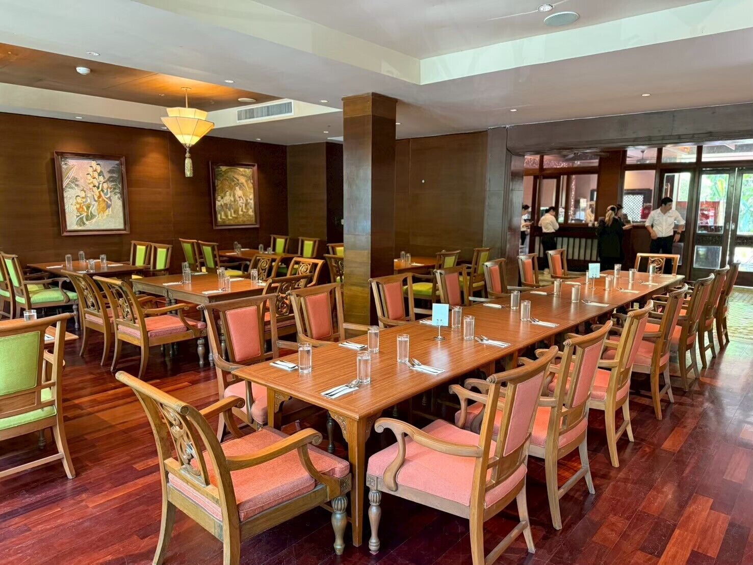 A spacious dining area with wooden tables and chairs, framed artwork on the walls, and a modern ceiling design.