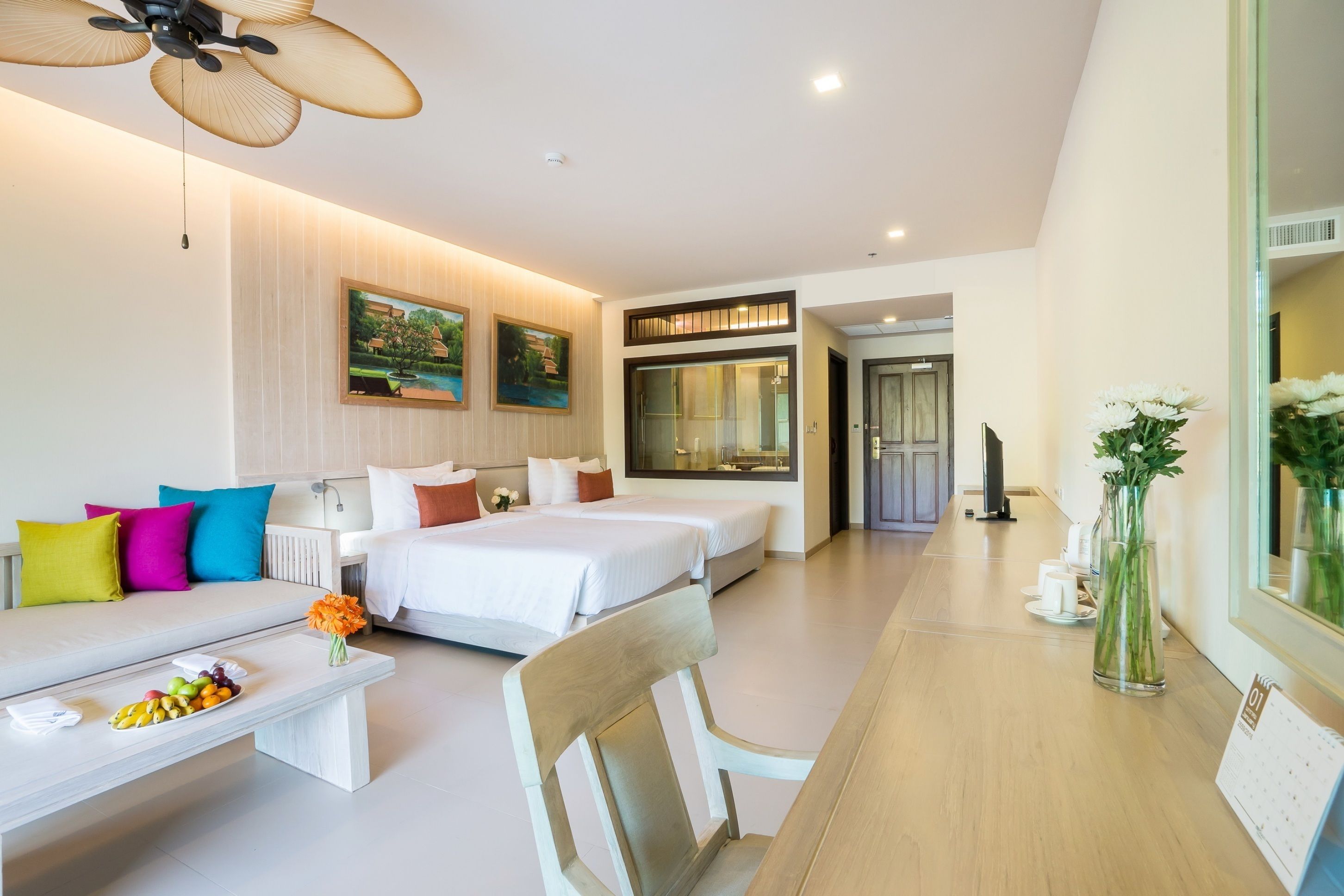 A modern hotel room with two beds, a sofa, a dining table, and a large window.
