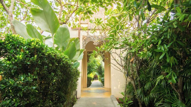 Un sendero serpentea a través de un exuberante jardín con una fuente central y un arco decorativo.