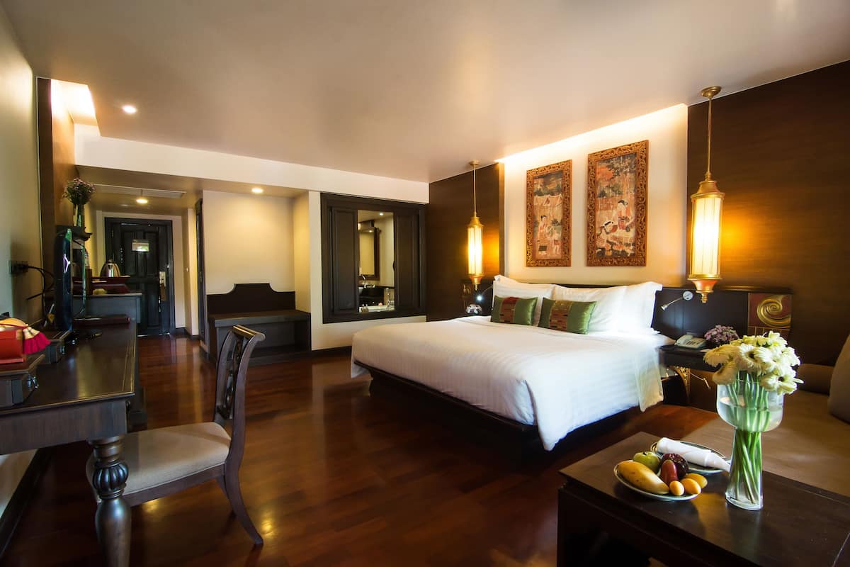 A hotel room with a large bed, bedside tables, a desk, and a dining area.