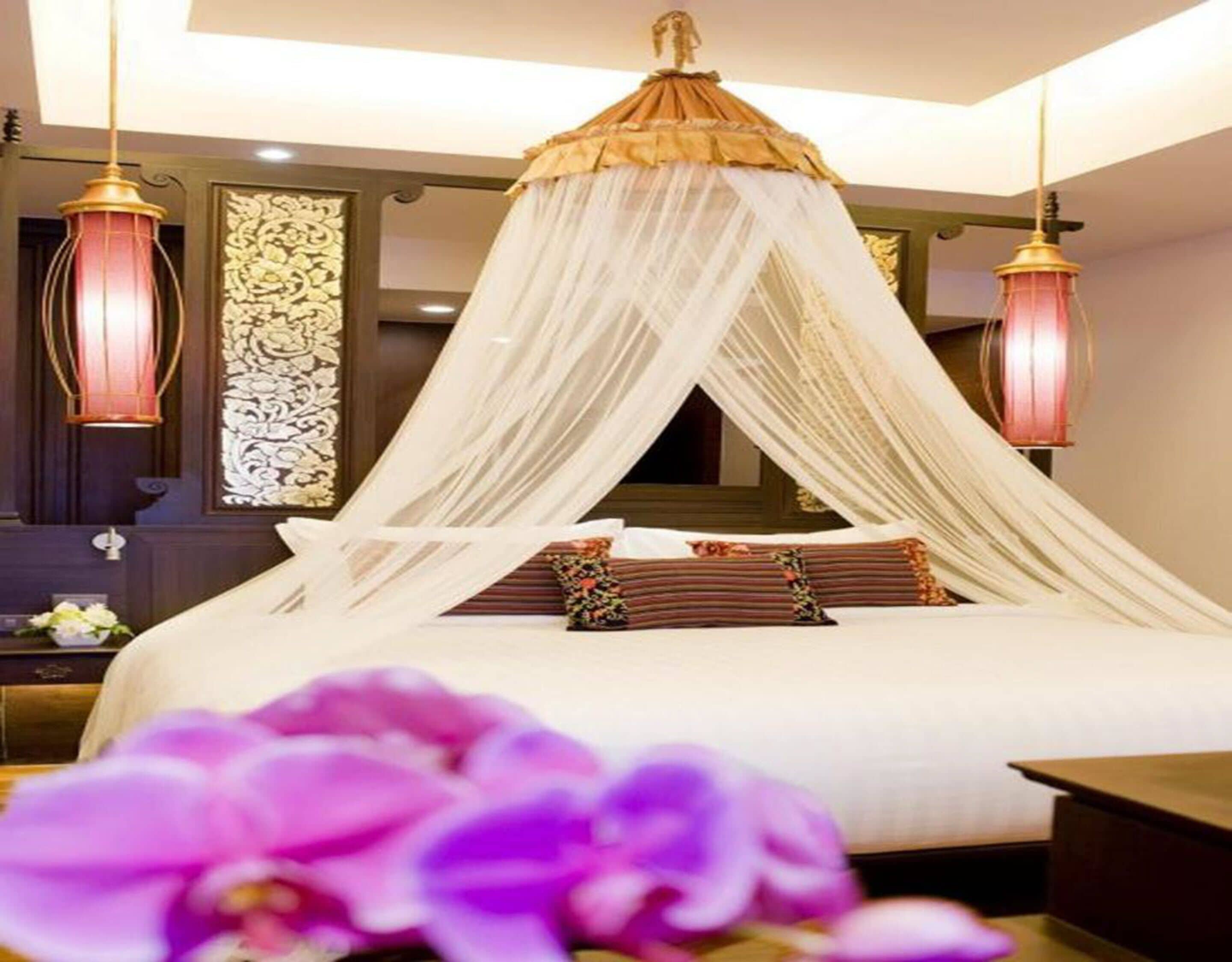 A bedroom with a canopy bed, two bedside lamps, and a decorative wall panel.