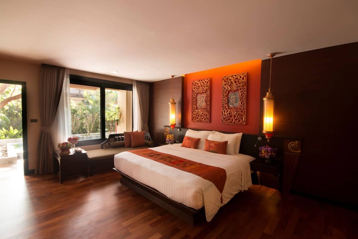 A spacious bedroom with a large bed, a bench, and a view of greenery outside.