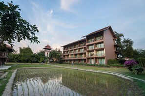 A multi-story hotel with a courtyard featuring a pond and a traditional pagoda in the background.