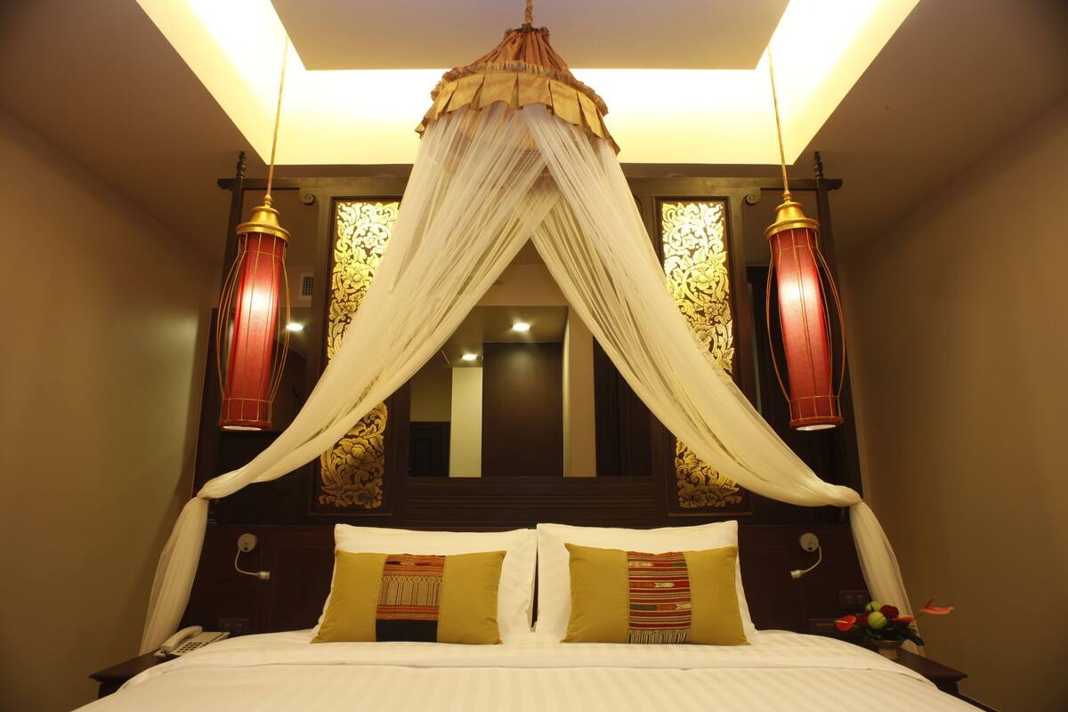 A bed with a canopy, two bedside tables, a telephone, and a mirror with ornate decorations.